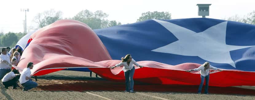 A flag crew tries to control a giant Texas flag in windy conditions during opening day of...