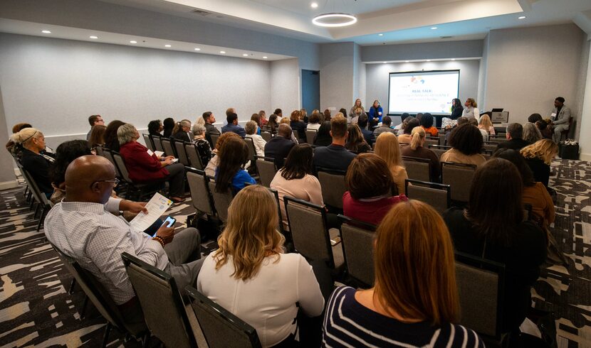 The audience sitting in chairs in a conference room with a screen at the front.