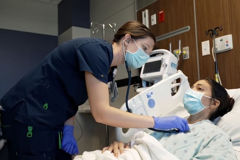 A nurse listens to the heartbeat of a patient laying in bed.