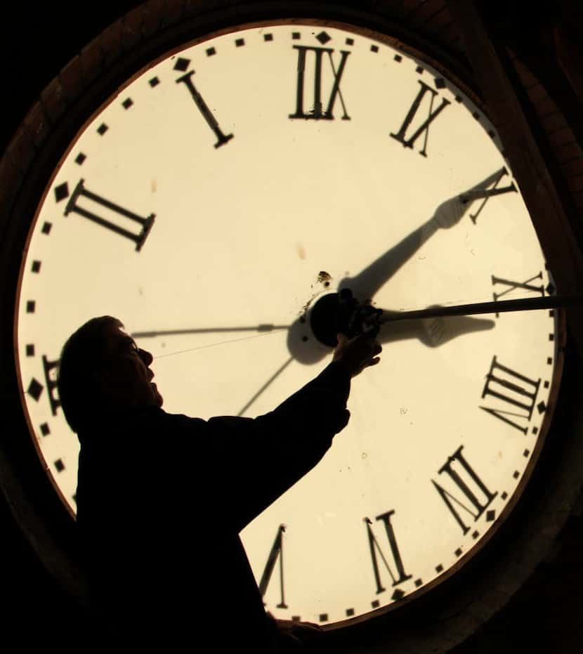 Custodian Ray Keen checks the time on a clock face after changing the time on the clock atop...