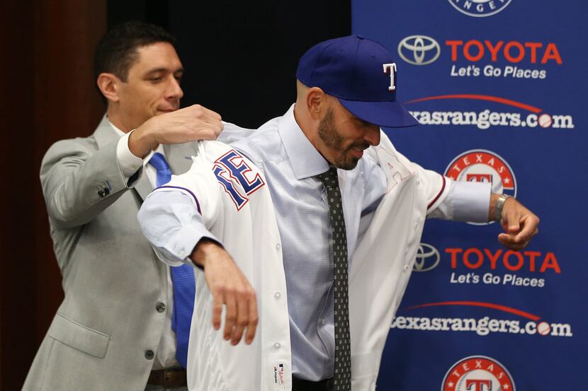 Texas Rangers' new manager Chris Woodward puts on his jersey with help from General Manager...