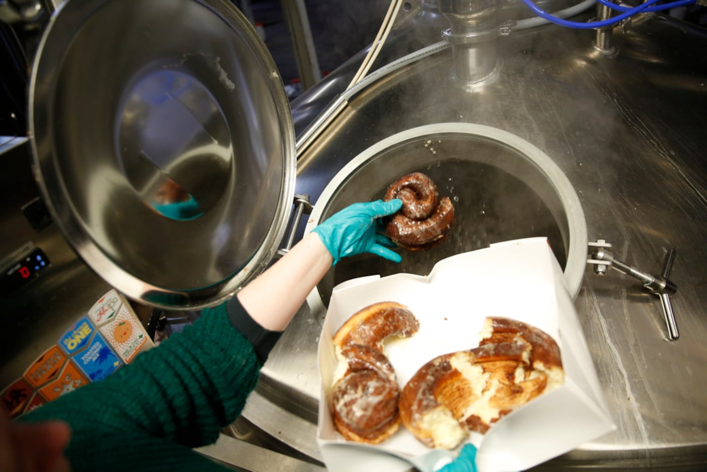 Brittany LaFollett, brand manager at 903 Brewers, drops cinnamon rolls into a fermenting...