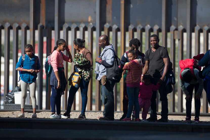 Un grupo de migrantes de Centroamérica espera junto a la barda fronteriza en El Paso, Texas,...