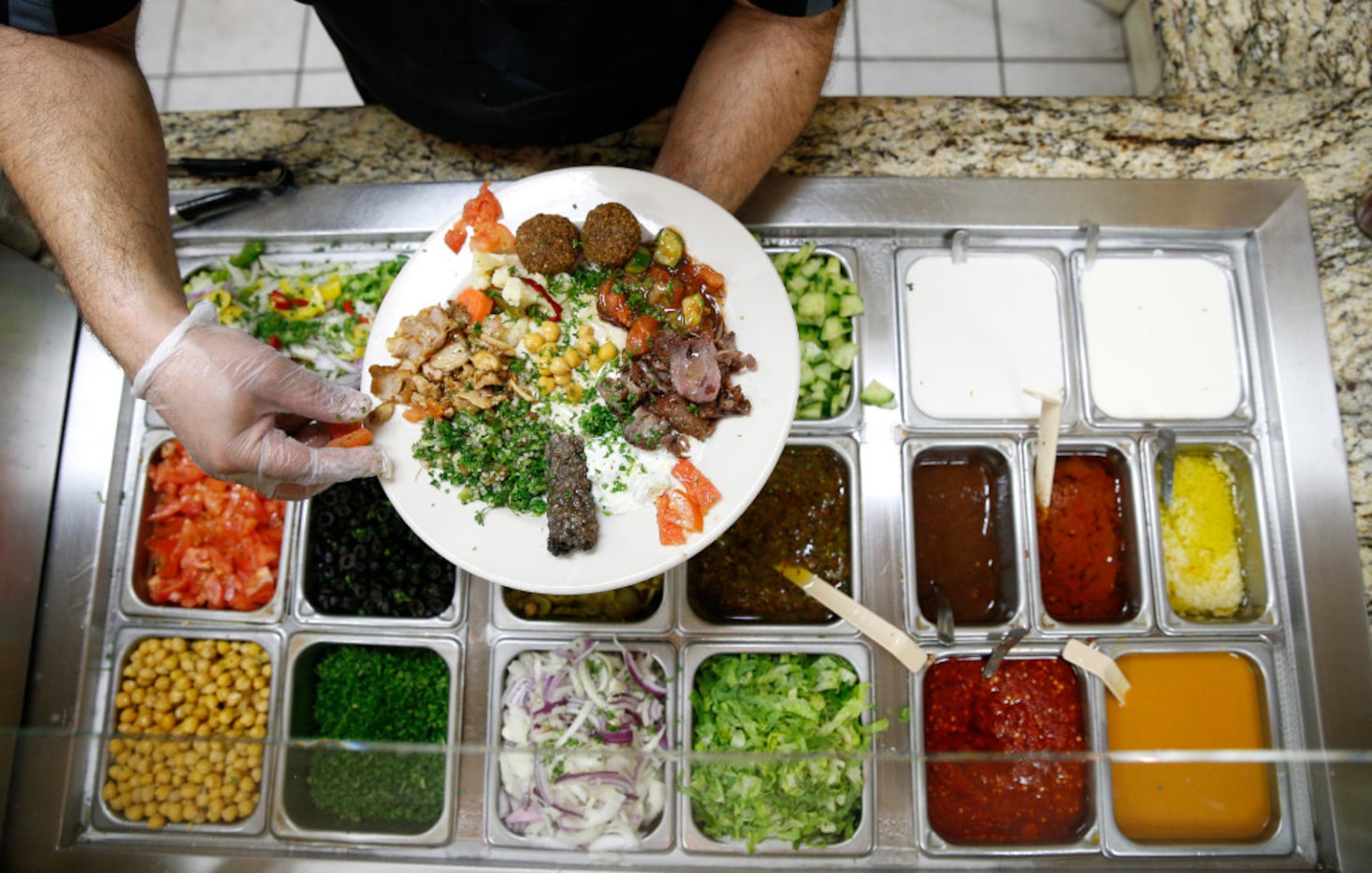 Fuad Al Bawyma prepares a plate of Iraqi food during the 'Breaking Bread' cultural exchange...