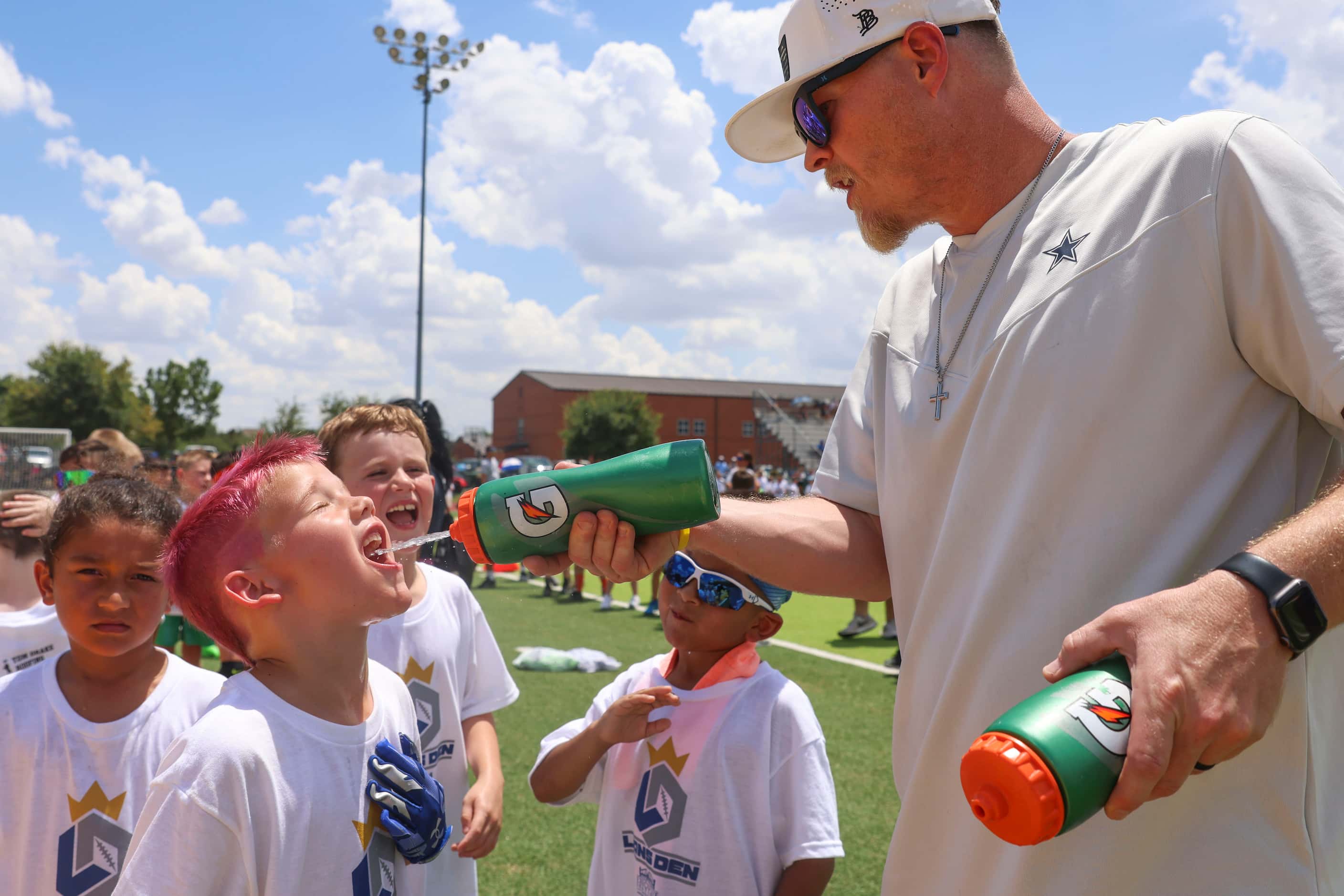 Volunteer Nathan Duran (right) sprays water on young football players as they line up to...