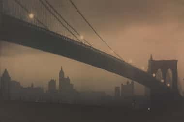 In Karl Struss' "Brooklyn Bridge, Nocturne," glowing lights trace an elegant path along the...
