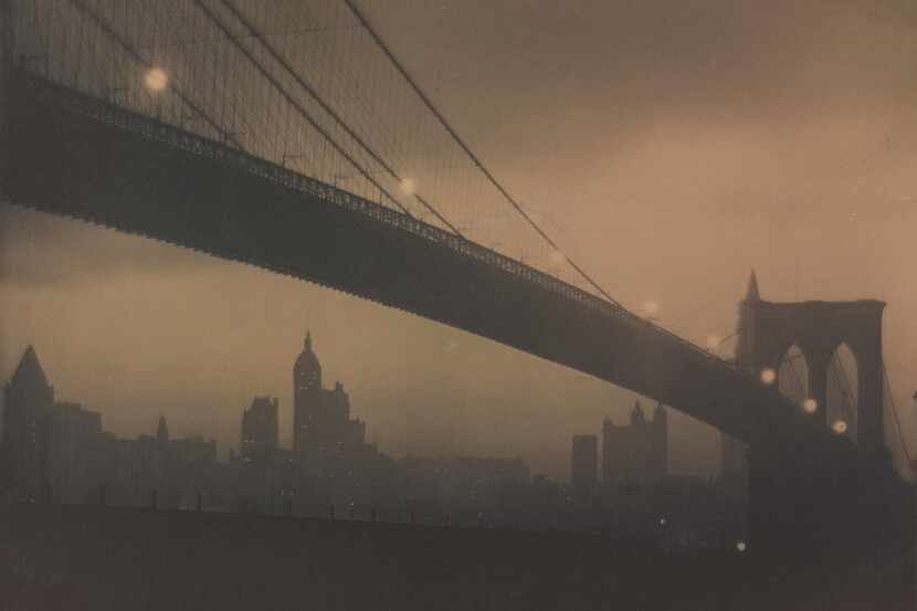 In Karl Struss' "Brooklyn Bridge, Nocturne," glowing lights trace an elegant path along the...