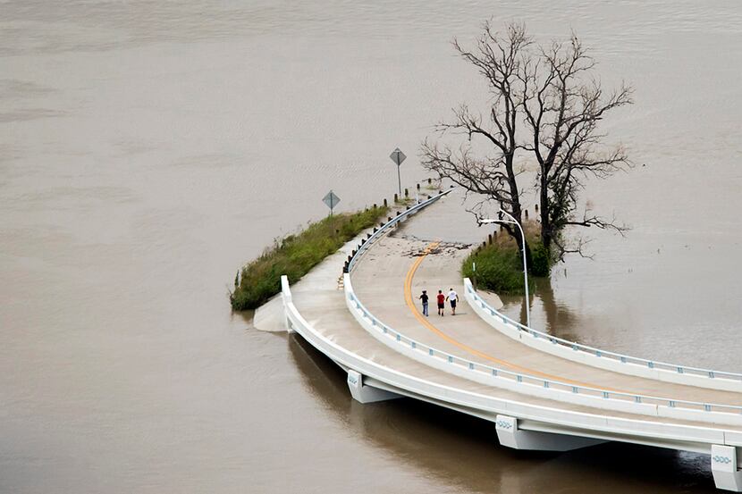  Flood waters from the swollen Trinity River surround a roadway as people walk from the...