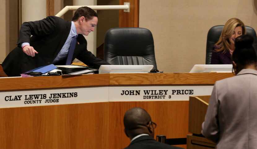 Dallas County Judge Clay Jenkins reaches for a paper near the empty seat of Dallas County...