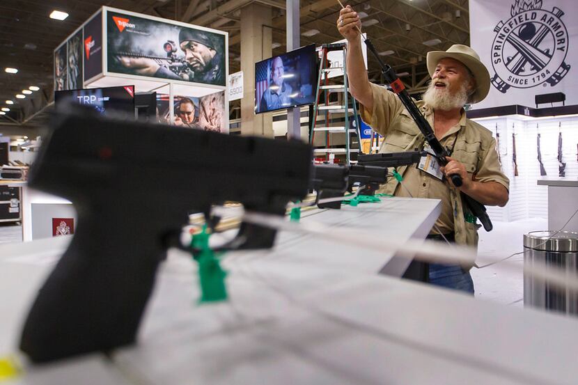 Jim Fleming uses a wooden dowel to ensure all display firearms lack a firing pin at a booth...
