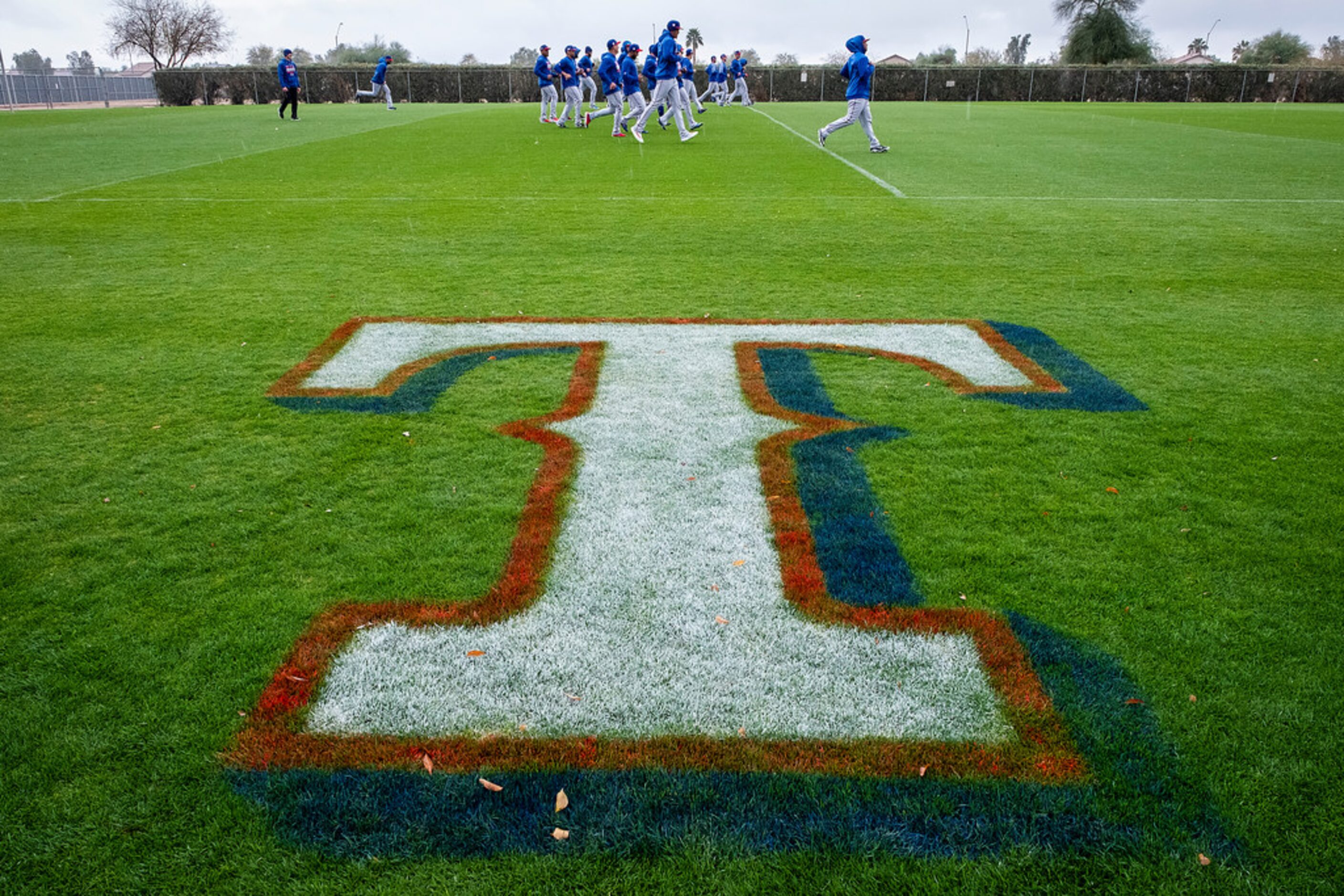 Texas Rangers position players run in the rain on a conditioning field during a spring...