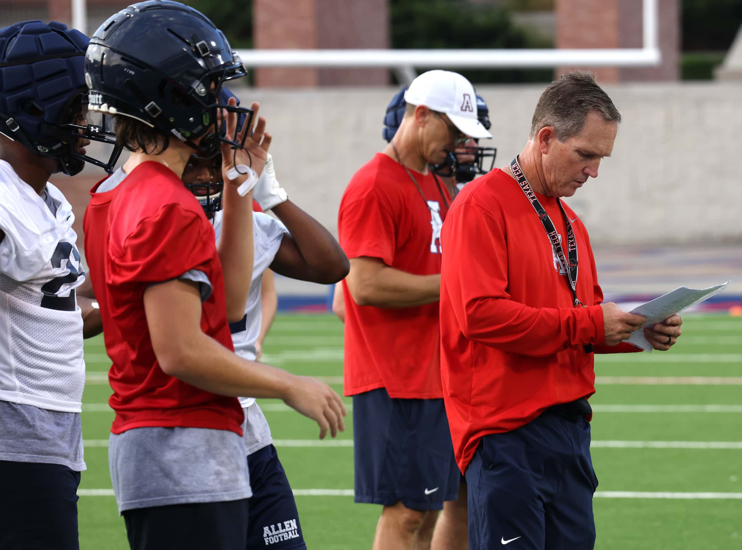 Allen head coach Lee Wiginton, right, looks over his list of plays during an early morning...