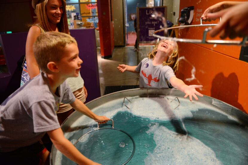 Chase Thomson, 5, reaches out to pop a giant bubble, while Caiden Thomson, 7, and Kelly...