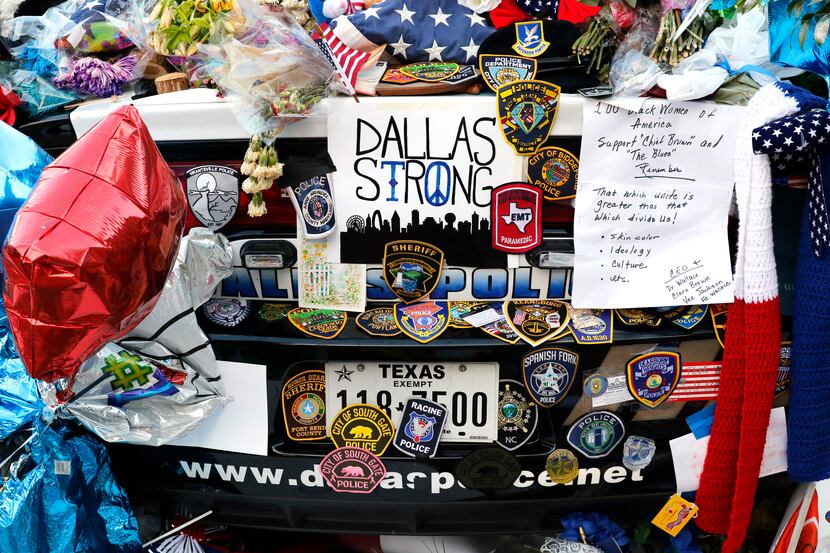 Two Dallas police patrol cars are covered with notes, flowers, balloons and other items as...