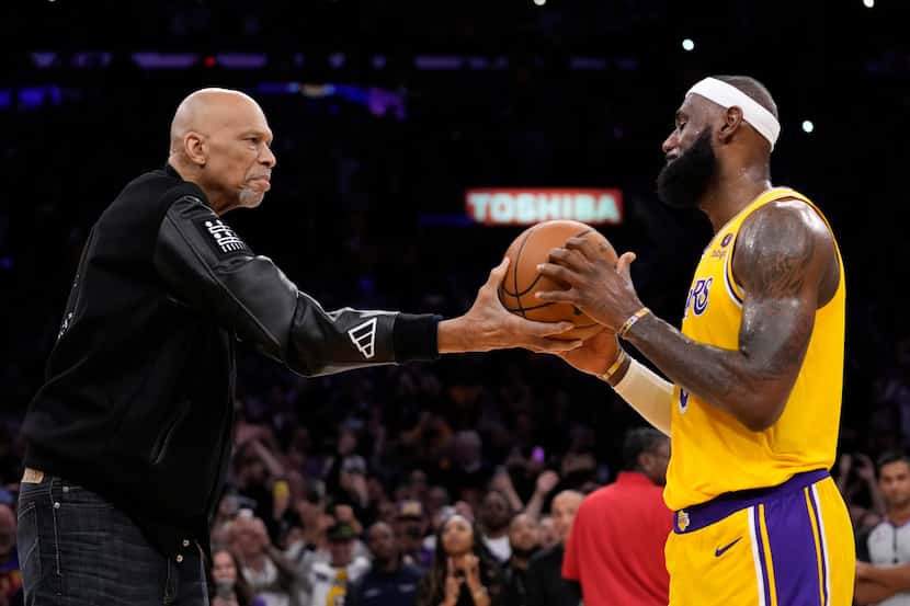 Kareem Abdul-Jabbar, left, hands the ball to Los Angeles Lakers forward LeBron James after...