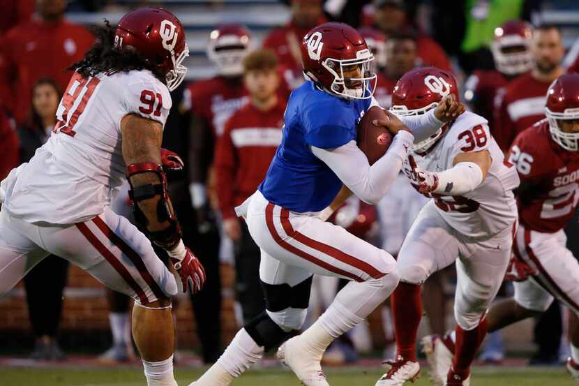 Oklahoma quarterback Jalen Hurts (1) carries between defenders Dillon Faamatau (91) and...