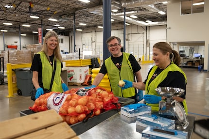 Three volunteers in safety vests stand around a table sorting food donations, including two...