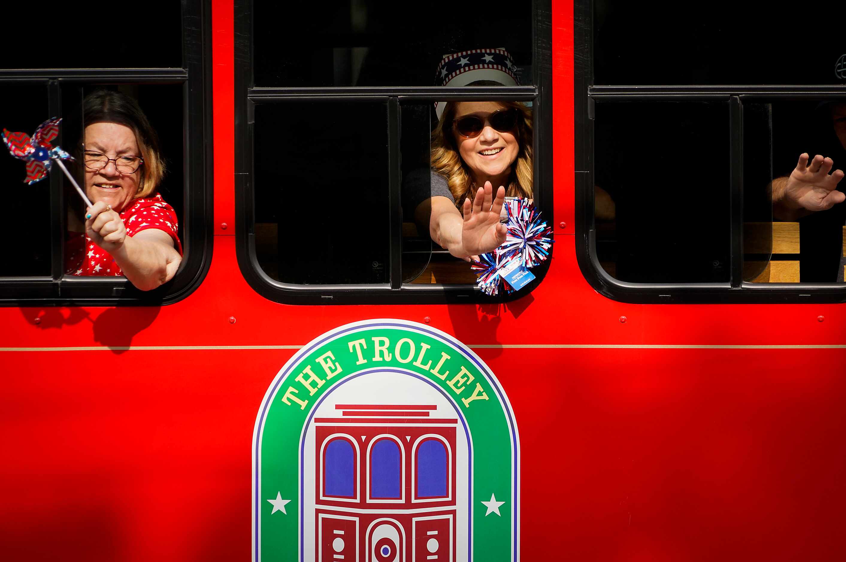 People wave from the Arlington Trolley during the Arlington Independence Day Parade on...