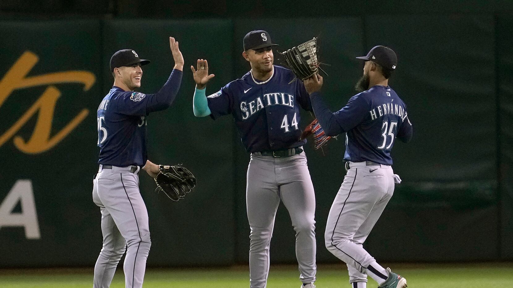 Seattle Mariners' Dylan Moore, left, celebrates with Julio Rodriguez (44) and Teoscar...