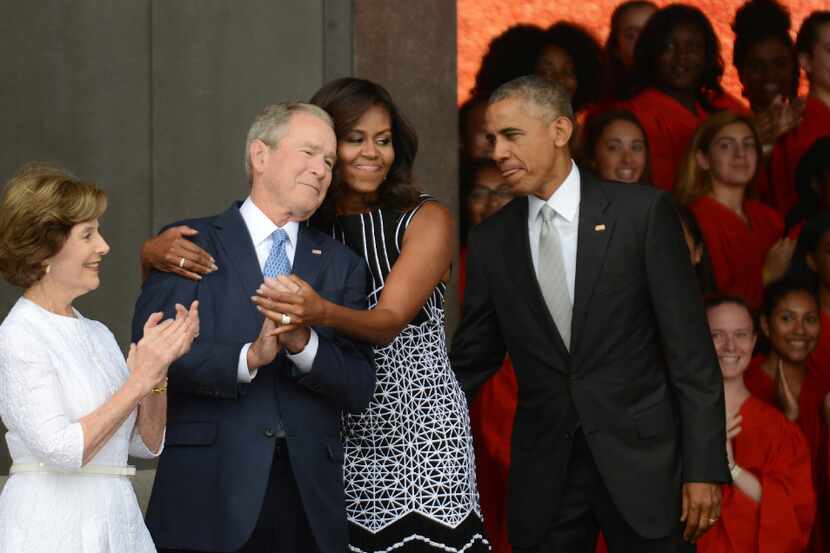 President Barack Obama watches first lady Michelle Obama embracing former president George...