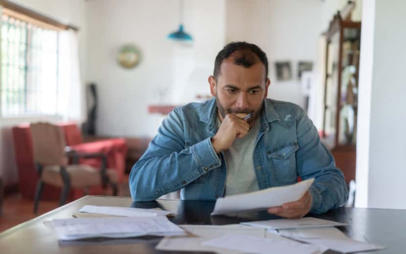 a man sits at his desk looking at bills.
