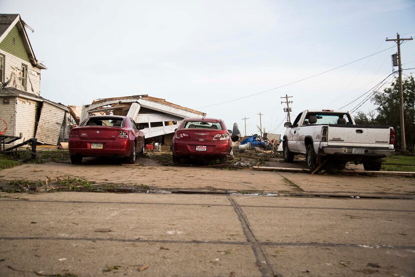 Damaged cars are parked in front of a garage that was torn down by a tornado on Monday, June...