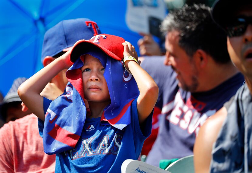 Young Texas Rangers fan Ripken Echols takes cover from the searing sun as he watches his...