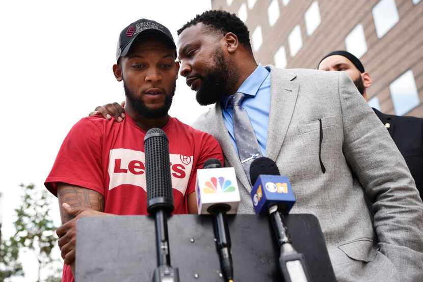 Attorney Lee Merritt whispers to Lyndo Jones during a news conference outside the Frank...