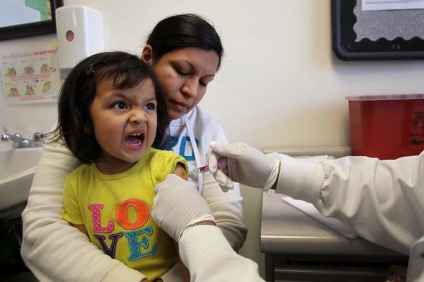 Irene Rangel, 2, with her mother Roxana Palacios, gets a flu shot from RN Pat Cook at the...
