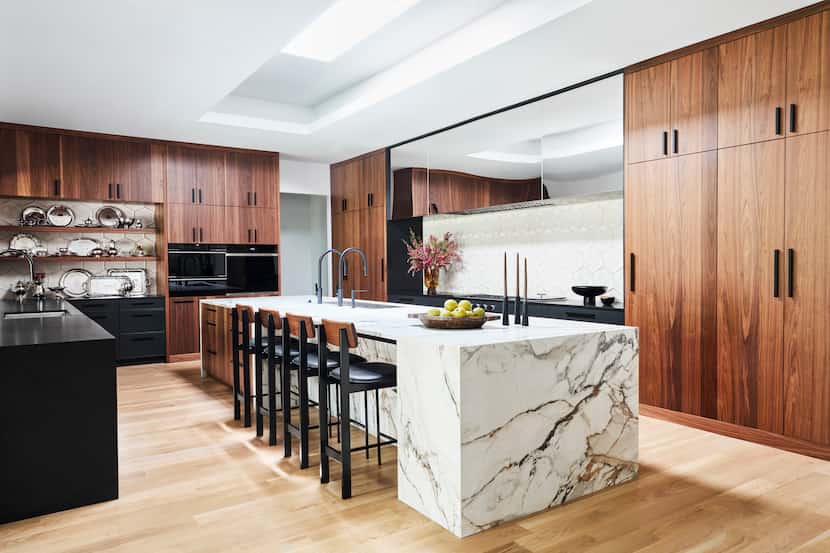 Large center island with countertop seating has a waterfall edge, wood cabinets, silver...