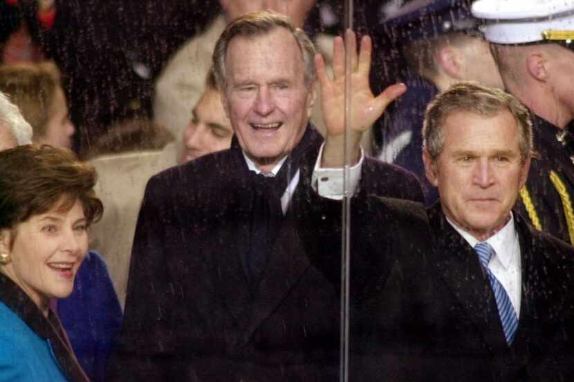  In this Jan. 20, 2001, photo, standing in the rain, President George W. Bush waves as he...