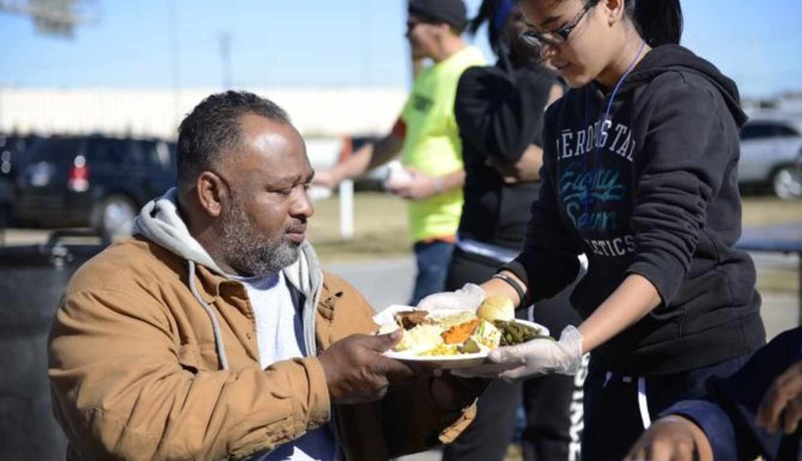 La voluntaria Nancy Morataya, de 13 años, ofrece un plato de comida a Howard B. Bates Sr.,...