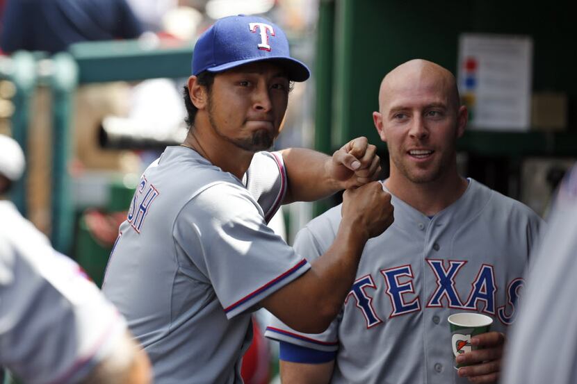 Texas Rangers starting pitcher Yu Darvish, left, mimics batting in the dugout with catcher...