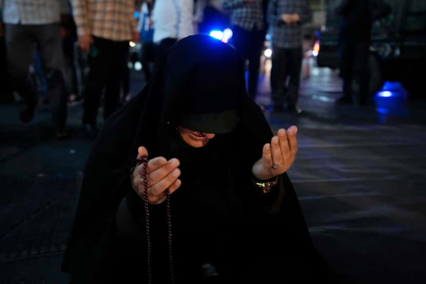An Iranian woman prays for President Ebrahim Raisi in a ceremony at Vali-e-Asr square in...