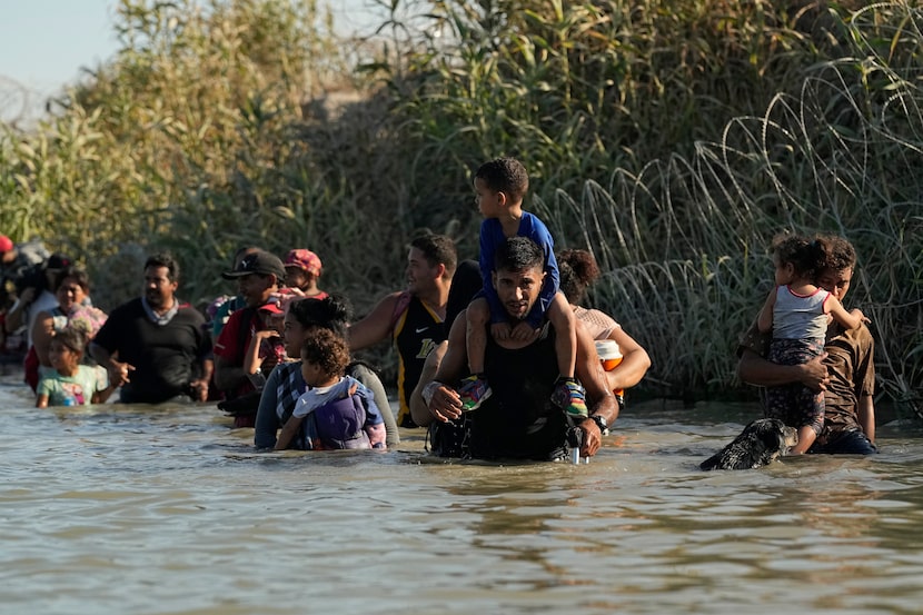 Migrants navigate around concertina wire along the banks of the Rio Grande after crossing...