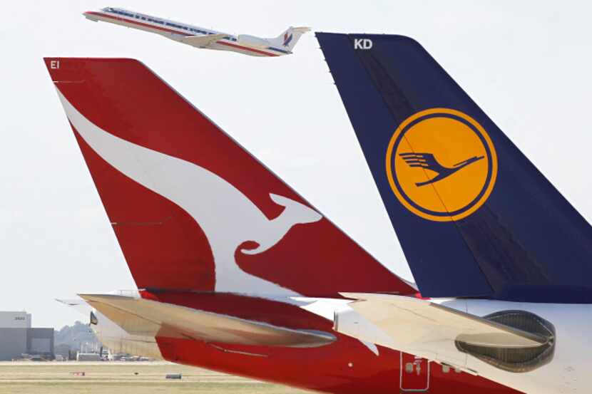 An American Eagle flight takes off behind Qantas and Lufthansa international planes parked...