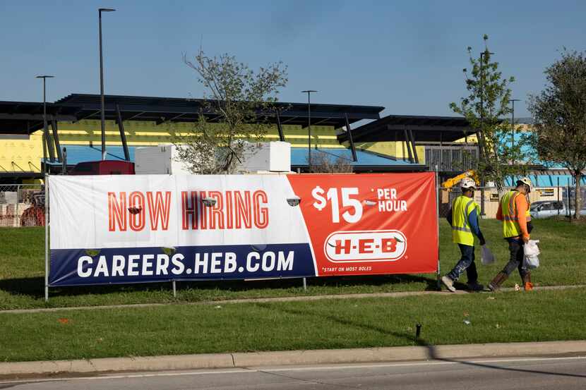 Construction workers walk by a hiring sign outside the H-E-B store under construction at...