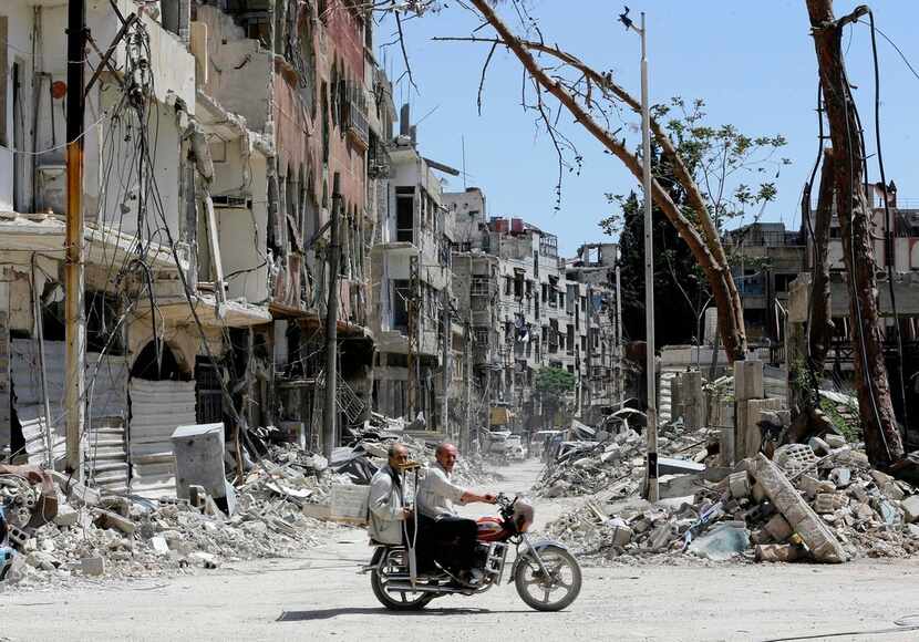 Syrians ride a motorbike along a destroyed street in Douma on the outskirts of Damascus on...