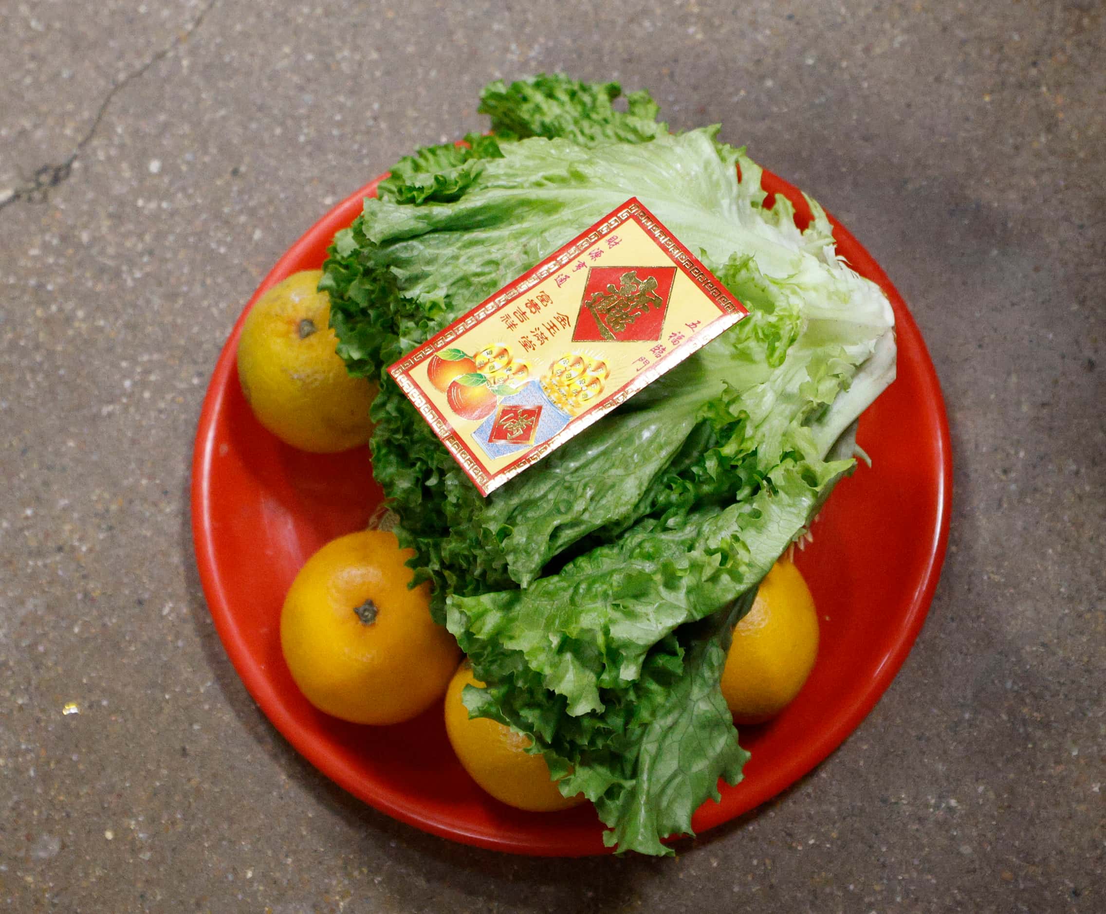 Oranges, lettuce and a red envelope are placed on the ground before lion dance during a Luna...