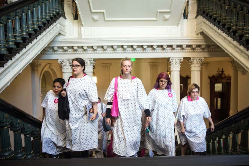Planned Parenthood supporters, dressed in hospital gowns, walk up the stairs of the State...