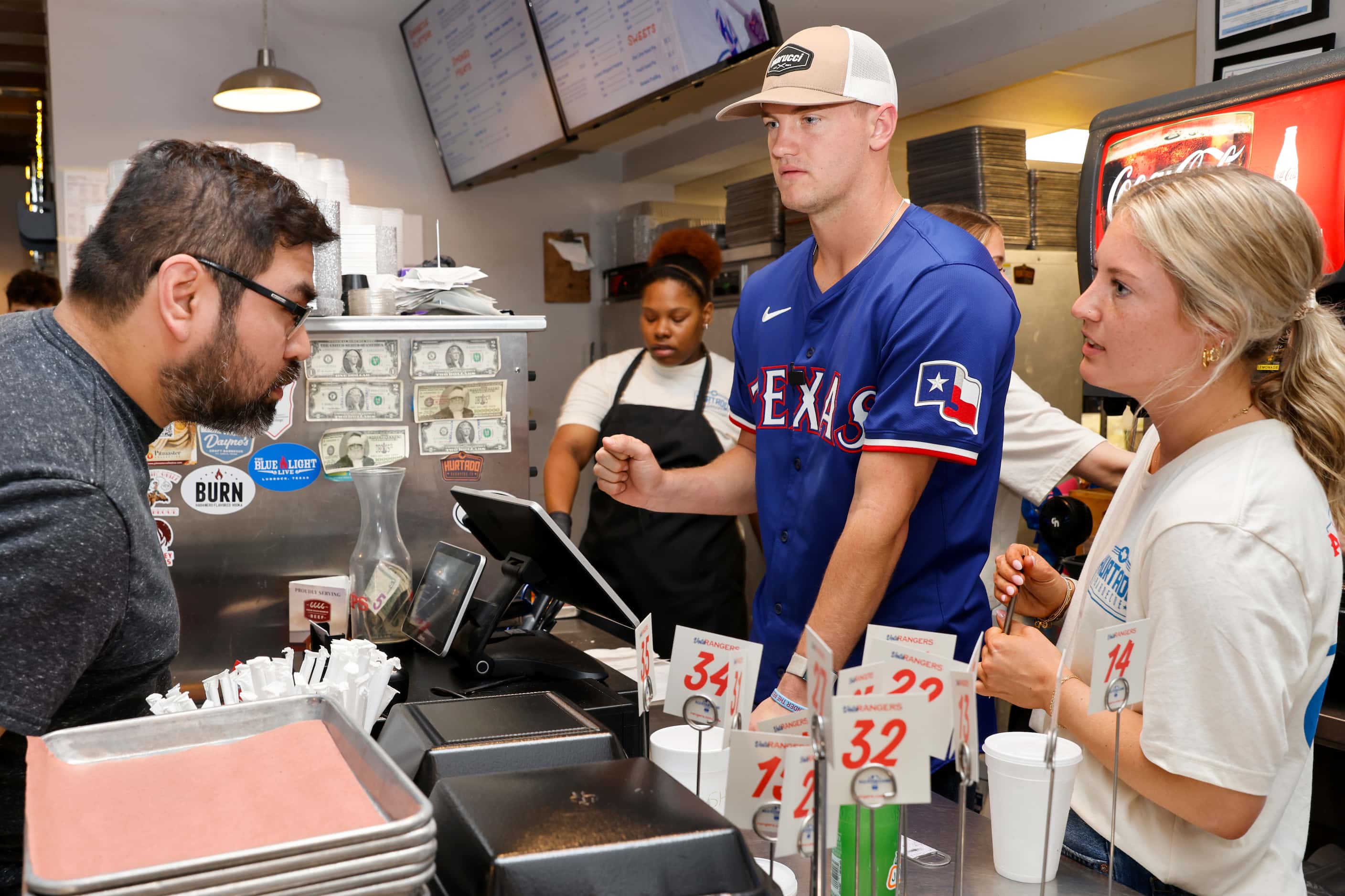 Texas Rangers third baseman Josh Jung listens to a customer as he takes an order behind the...