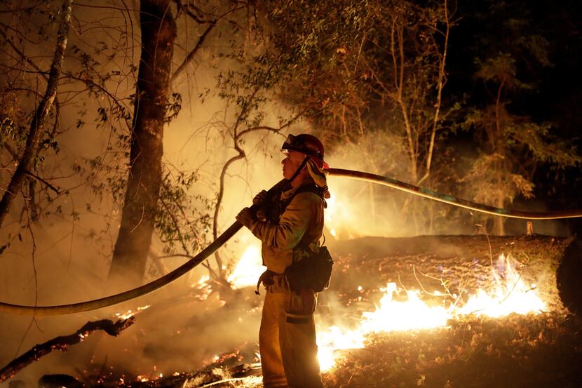 A firefighter holds a water hose while fighting a wildfire in Santa Rosa, Calif.