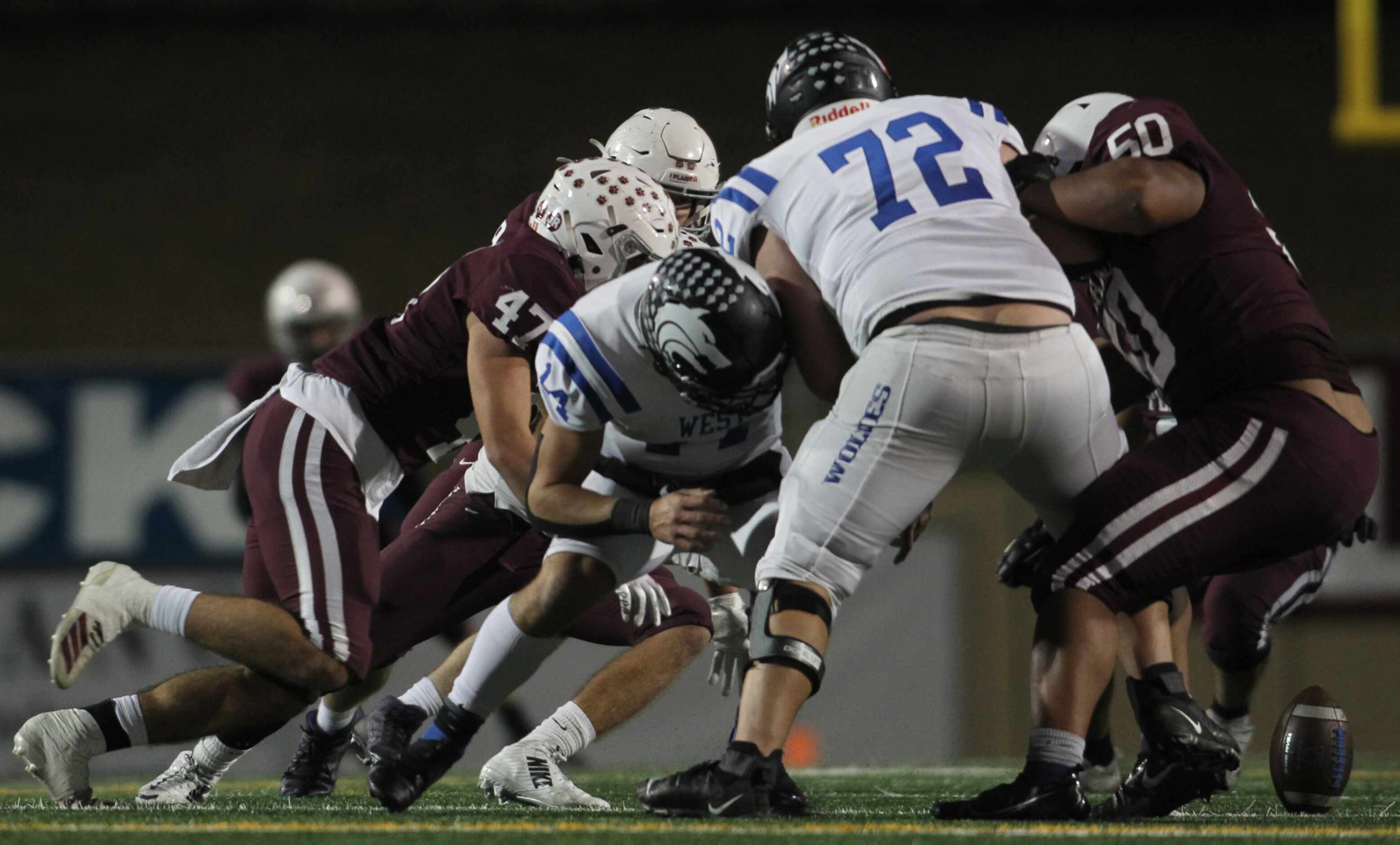 Plano West quarterback Vance Feuerbacher (14), center, is hit in the backfield and fumbled...