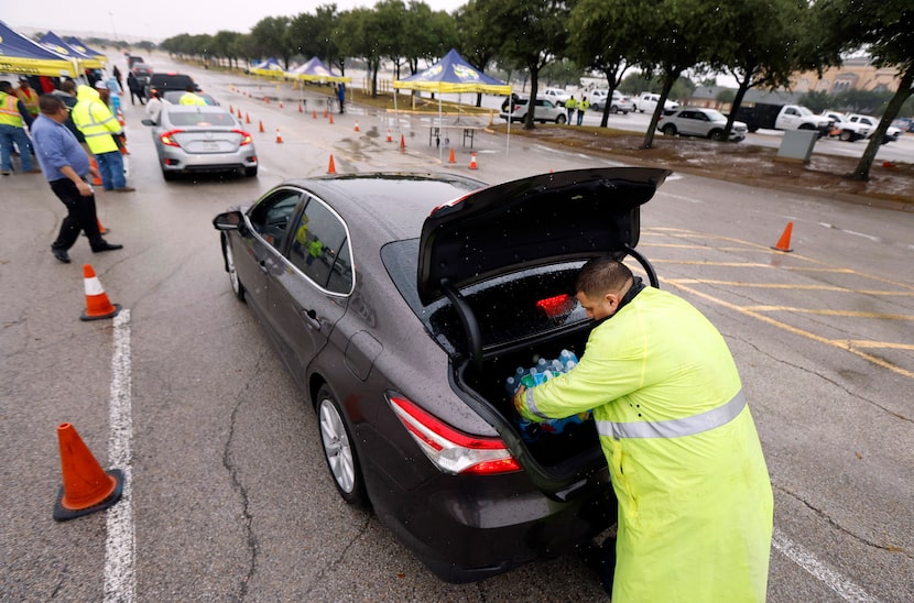 Grand Prairie employee Omar Esquivel loads bottled water for a waiting resident in line at...