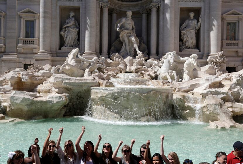 Tourists throw their coins in the Trevi Fountain in Rome. The fountain is featured in...