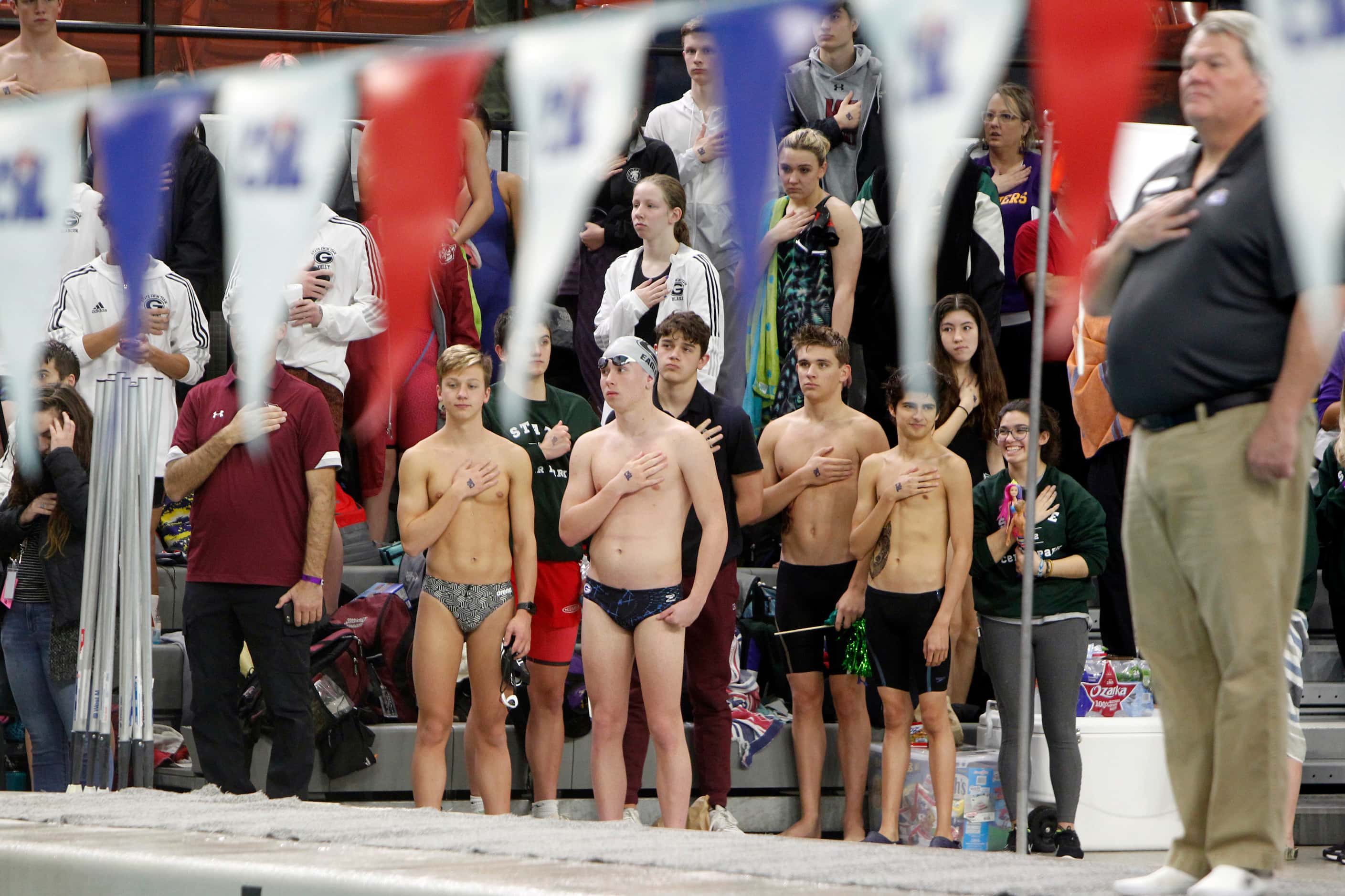Swimmers and fans pause behind a UIL official for the playing of the national anthem. The...
