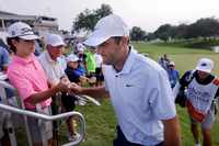 Golfer Scottie Scheffler fit bumps a fan after completing his opening round in the Charles...