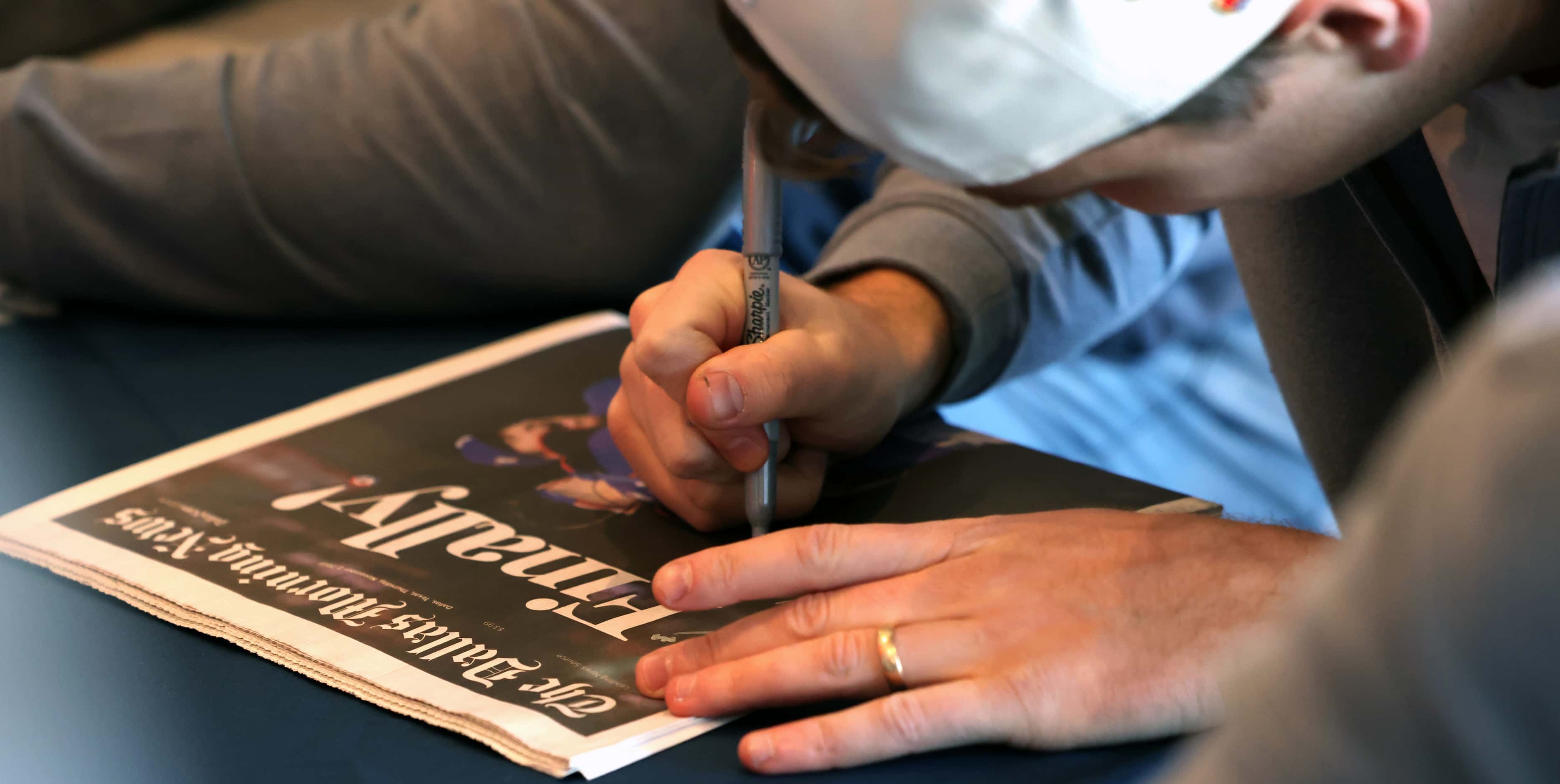 Texas Rangers pitcher Josh Sborz autographs a souvenir cover of a special newspaper section...