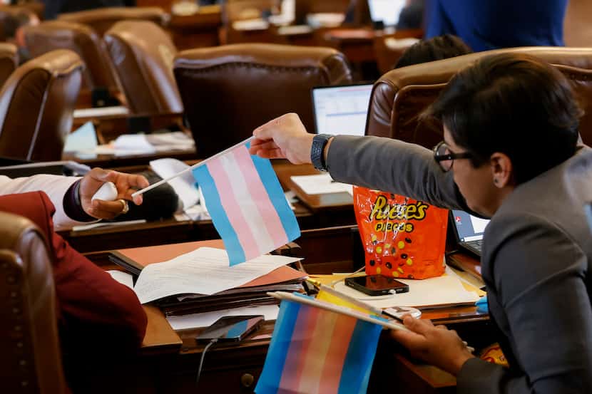 Two lawmakers exchange a transgender pride flag in the House chamber in Austin on Thursday,...