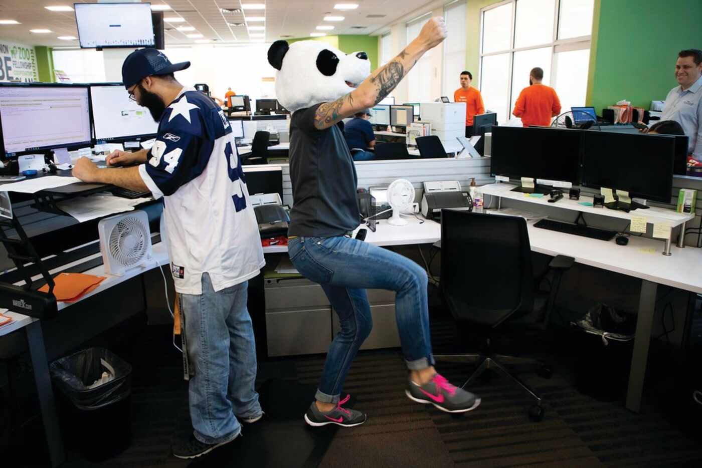 Wearing a panda head, Brandi Beakley dances near the desk of Cameron Ratcliff at...